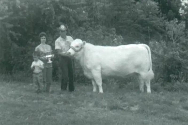 The Laue family standing next to a White Charolais bull and holding up a trophy